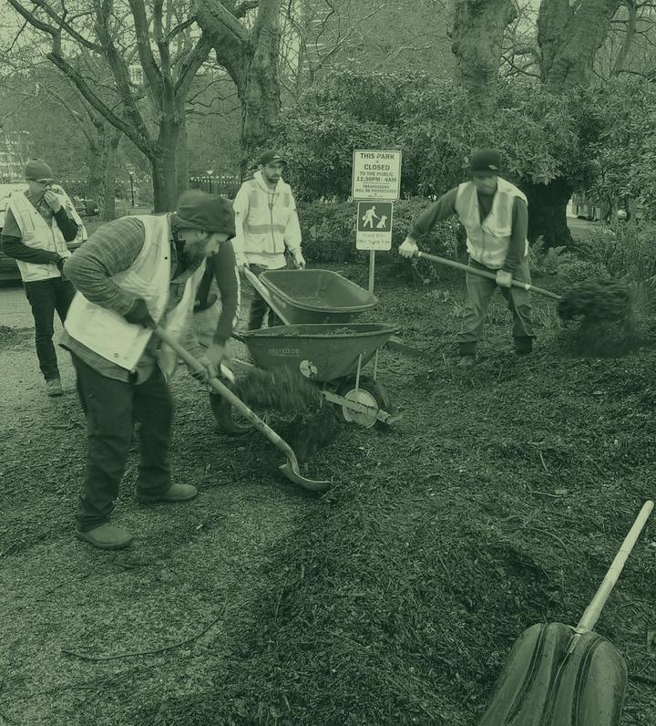 A park crew in hi-vis spreading mulch from a wheelbarrow, in green duotone.