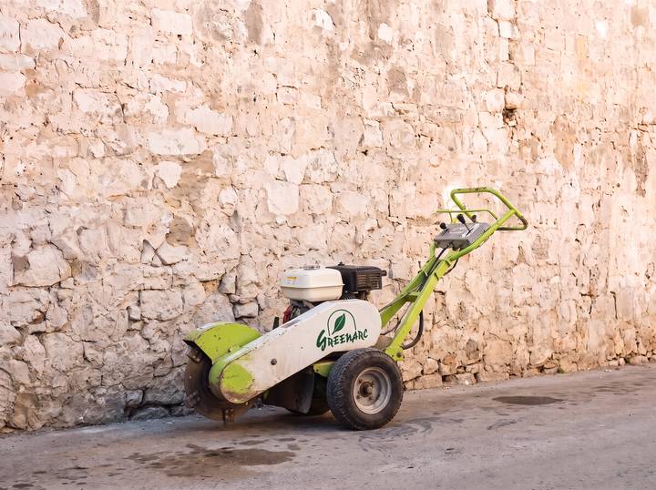 Compact white stump grinder with a lime-green cutter guard and the Greenarc logo, against a limestone wall.