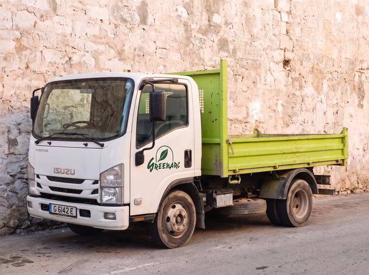 White 7.5 tonne tipper truck with a lime-green body and the Greenarc logo on the door, against a limestone wall.