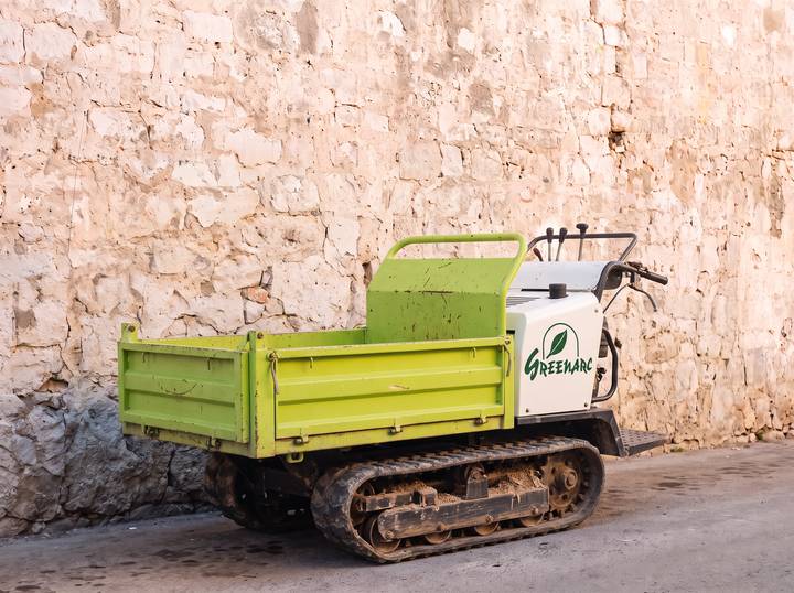 White tracked dumper with a lime-green skip and the Greenarc logo, against a limestone wall.